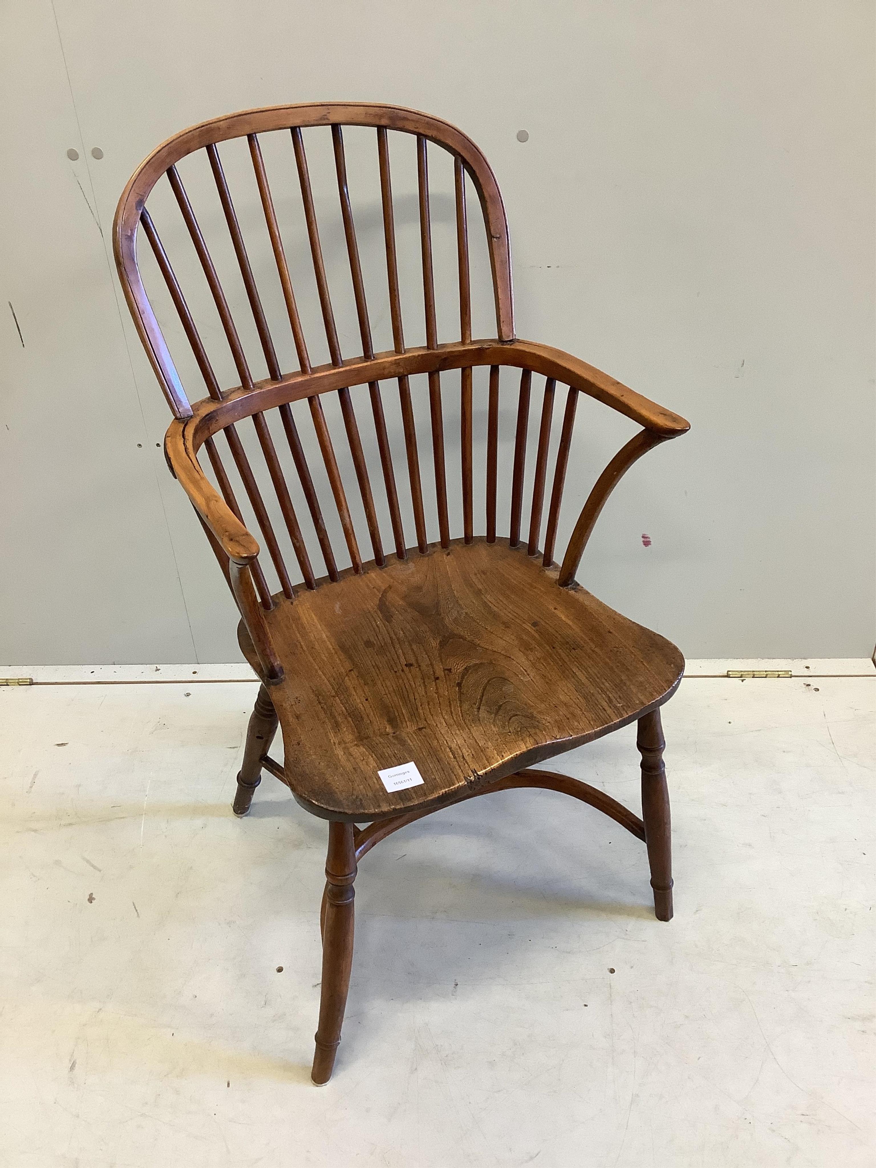 An early 19th century yew and elm comb back Windsor elbow chair with crinoline stretcher, width 53cm, depth 42cm, height 99cm. Condition fair, arm rail split to left side, left leg now misshapen with minor chips.